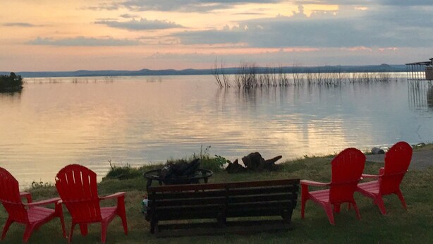 Vista del lago con sillones Adirondack rojos y un banco de madera mirando al agua.