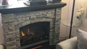 Una sala de estar con chimenea de piedra, un televisor de pantalla plana sobre un soporte negro y una lámpara de pie moderna.