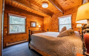 Une chambre dans une cabane en bois, avec un lit, deux fenêtres, un miroir et un luminaire au plafond.