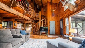 Interior acolhedor de uma cabana com escada de madeira, televisão e lareira.