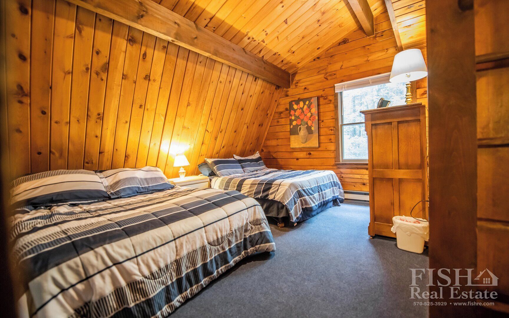 Une chambre confortable, aménagée dans le style d’un chalet, avec deux lits, des murs en bois, une fenêtre et une lampe.