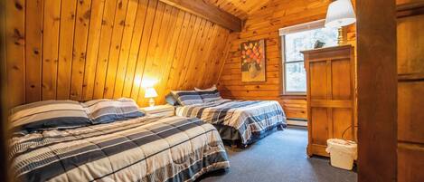 Une chambre confortable, aménagée dans le style d’un chalet, avec deux lits, des murs en bois, une fenêtre et une lampe.