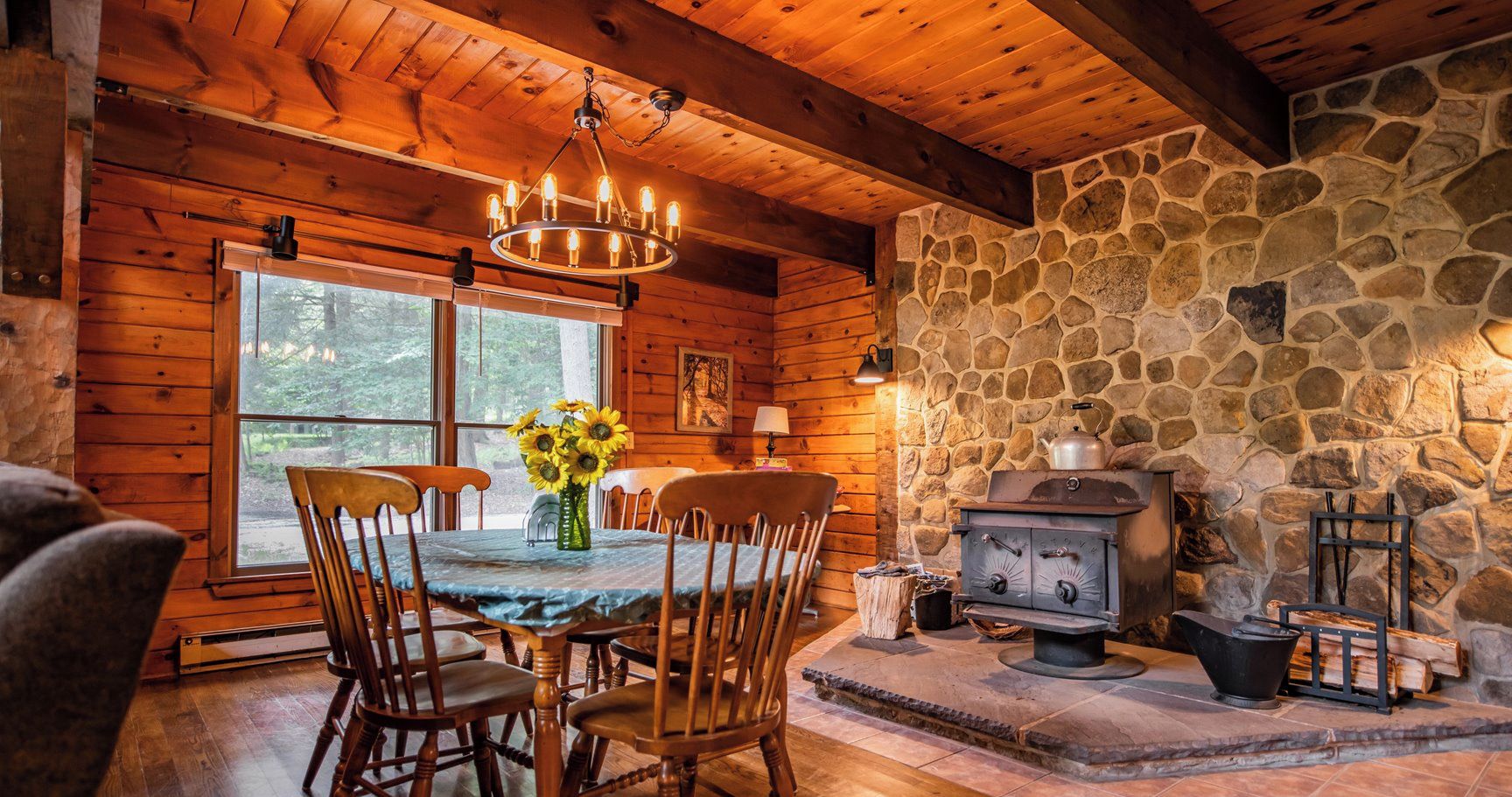 Un acogedor interior de cabaña con chimenea de piedra, mesa de comedor de madera y sillas.