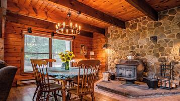 Un acogedor interior de cabaña con chimenea de piedra, mesa de comedor de madera y sillas.