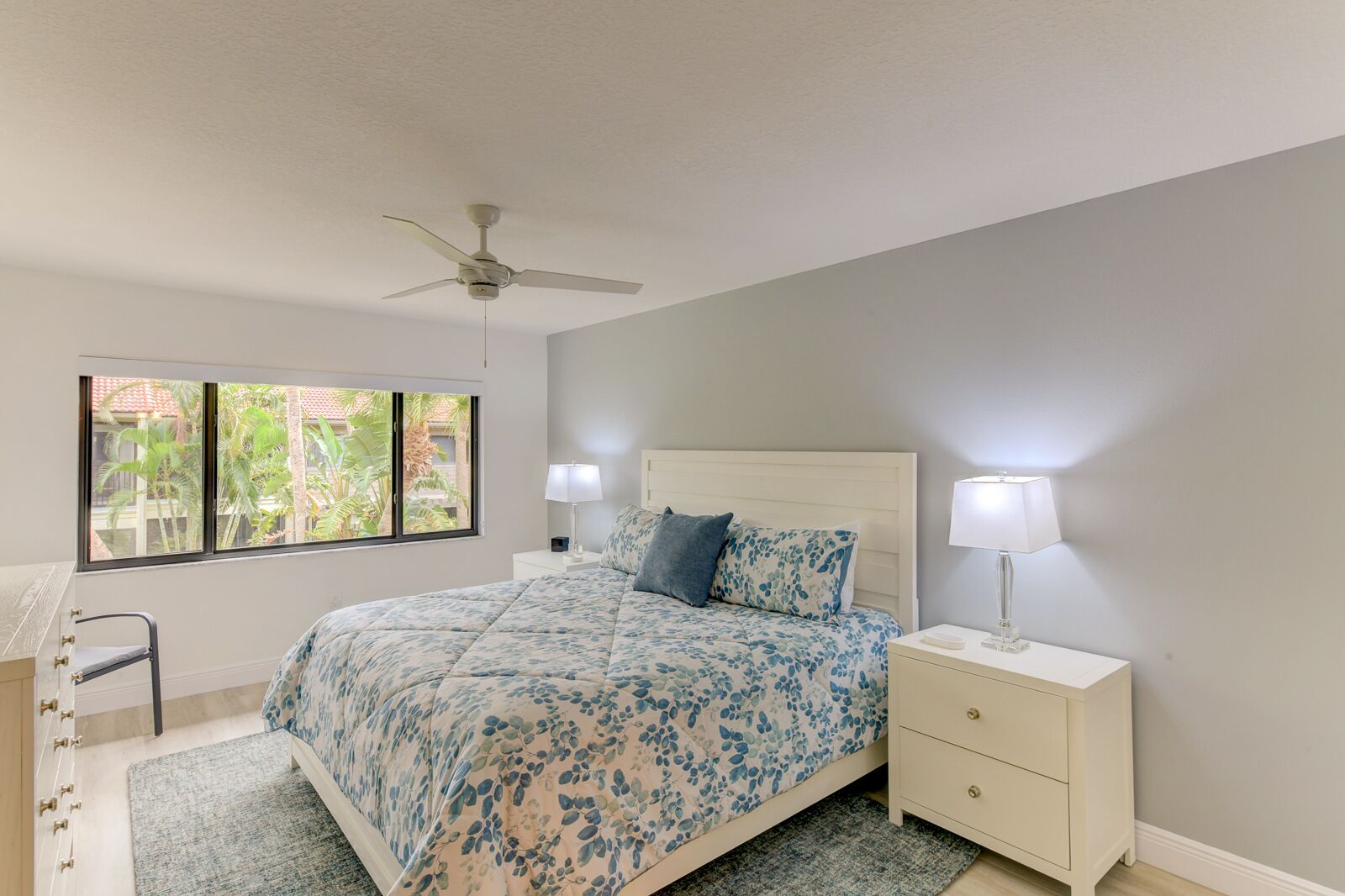A bedroom with a bed, nightstands, a desk, a chair, and a ceiling fan.