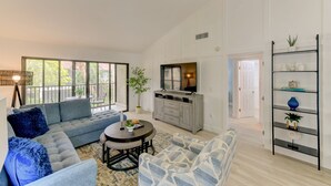 A spacious living room with a grey sofa, a round coffee table, and a TV stand.