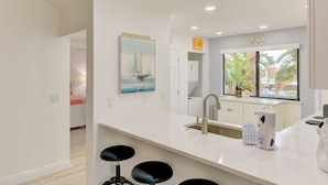 A modern kitchen with a large window, a sink, and a bar stool area.