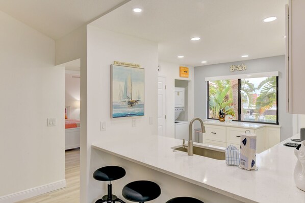 A modern kitchen with a large window, a sink, and a bar stool area.