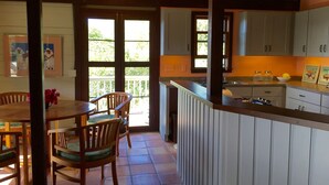 A kitchen with wooden cabinets, a dining area with a table and chairs, and a view of the outdoors through a glass door. - Private cottage in great location with a Path to Chocolate Hole Beach (St. John)