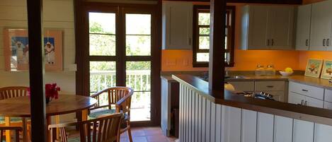 Cozinha com armários de madeira, área de jantar com mesa e cadeiras, e vista para o exterior através de uma porta de vidro.