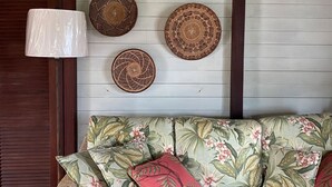 A room with a wooden wall, a woven wall hanging, a wicker sofa, and a white lamp. - Private cottage in great location with a Path to Chocolate Hole Beach (St. John)