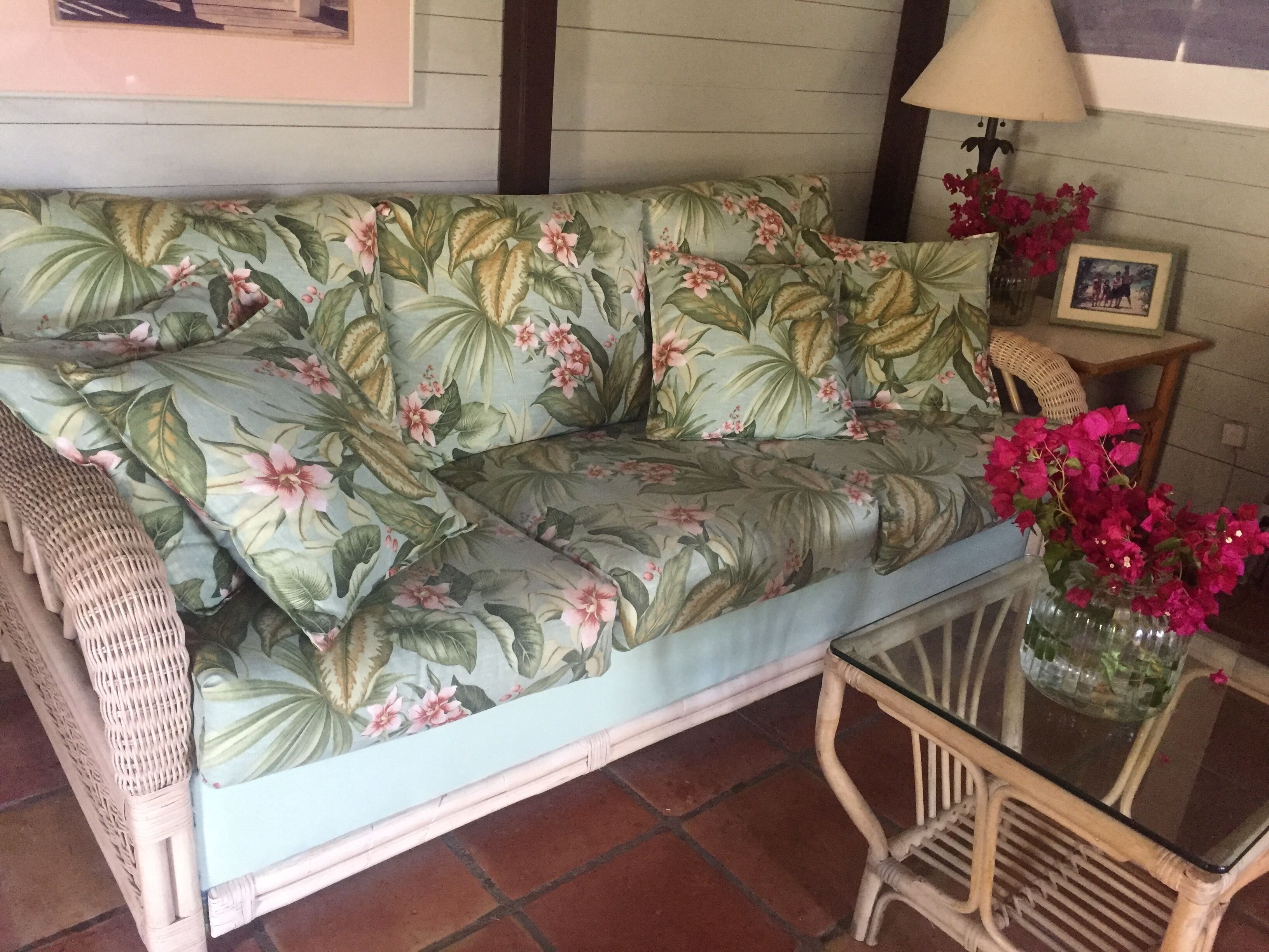 En sofa med blomstermønster, et glasbord og fletstole.