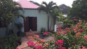 A house with a pink roof, a dog sitting on the steps, and a garden with pink flowers. - Private cottage in great location with a Path to Chocolate Hole Beach (St. John)