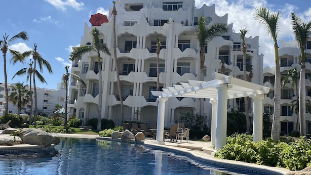 A resort with a swimming pool, palm trees, and a white building with balconies. - Our gem on the beach. (San José del Cabo)