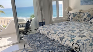 A bedroom with a bed, a bench, a view of the beach, and a window. - Our gem on the beach. (San José del Cabo)