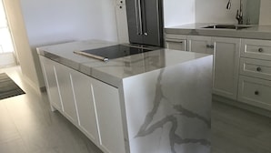 A modern kitchen with a marble countertop, stainless steel appliances, and white cabinetry. - Our gem on the beach. (San José del Cabo)