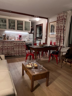 Uma sala de estar aconchegante com uma mesa de centro de madeira, uma mesa de jantar com cadeiras vermelhas e uma área de cozinha com armários e geladeira.