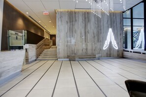 Un espace d’accueil moderne doté d’un comptoir de réception en marbre, d’un escalier et d’une grande fenêtre offrant une vue sur l’extérieur.