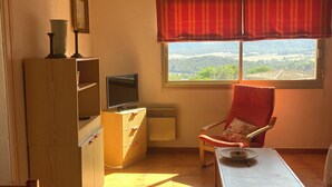 A cozy room with a wooden cabinet, a television, a red chair, and a window with a view of greenery. - SUPERB SEA VIEW over SANTA GIULIA bay in residence with private pool (Porto-Vecchio)