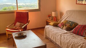 A cozy room with a wooden table, a red chair, a sofa with colorful cushions, and a window offering a view of the countryside. - SUPERB SEA VIEW over SANTA GIULIA bay in residence with private pool (Porto-Vecchio)
