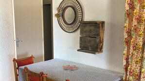 A dining area with a wooden table and chairs, a decorative mirror, and a floral curtain. - SUPERB SEA VIEW over SANTA GIULIA bay in residence with private pool (Porto-Vecchio)