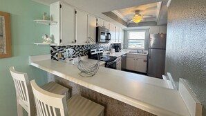 A compact kitchen with white cabinets, a black microwave, a stainless steel refrigerator, and a window with a view. - El Matador 451 - FREE TICKETS!! Your stay includes free tickets to many area attractions! (Fort Walton Beach)