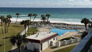 A pool area with a view of the ocean, palm trees, and a building with a red roof. - El Matador 451 - FREE TICKETS!! Your stay includes free tickets to many area attractions! (Fort Walton Beach)