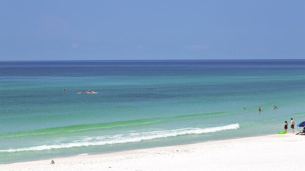 Ein Strand mit klarem türkisblauem Wasser, einem sandigen Ufer und einigen Menschen im Wasser.