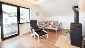 A modern living room with a black leather chair, a grey sofa, a wooden coffee table, and a black wood-burning stove. - Alpine Escape Near Lake Bled – Breathtaking Views & Nature Trails (Žirovnica)