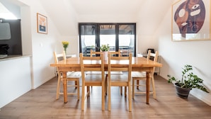 A dining area with a wooden table and chairs, a potted plant, and a large window with blinds. - Alpine Escape Near Lake Bled – Breathtaking Views & Nature Trails (Žirovnica)