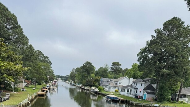 A waterfront view from a deck with a table and chairs, overlooking a calm river with houses and boats along the banks. - waterfront beach retreat with boat dock (Ocean Pines)