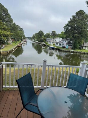 A waterfront view from a deck with a table and chairs, overlooking a calm river with houses and boats along the banks. - waterfront beach retreat with boat dock (Ocean Pines)
