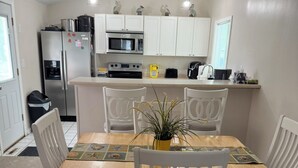 A dining area with a wooden table and white chairs, a potted plant, and a kitchen in the background with white cabinets and stainless steel appliances. - waterfront beach retreat with boat dock (Ocean Pines)