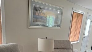 A living room with two grey sofas, a white side table, and a lamp. There is a framed picture on the wall and a window with blinds. - waterfront beach retreat with boat dock (Ocean Pines)