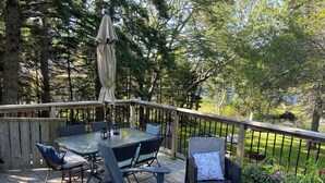 Une terrasse en bois avec une table à plateau de verre, des chaises en osier et un petit parasol.