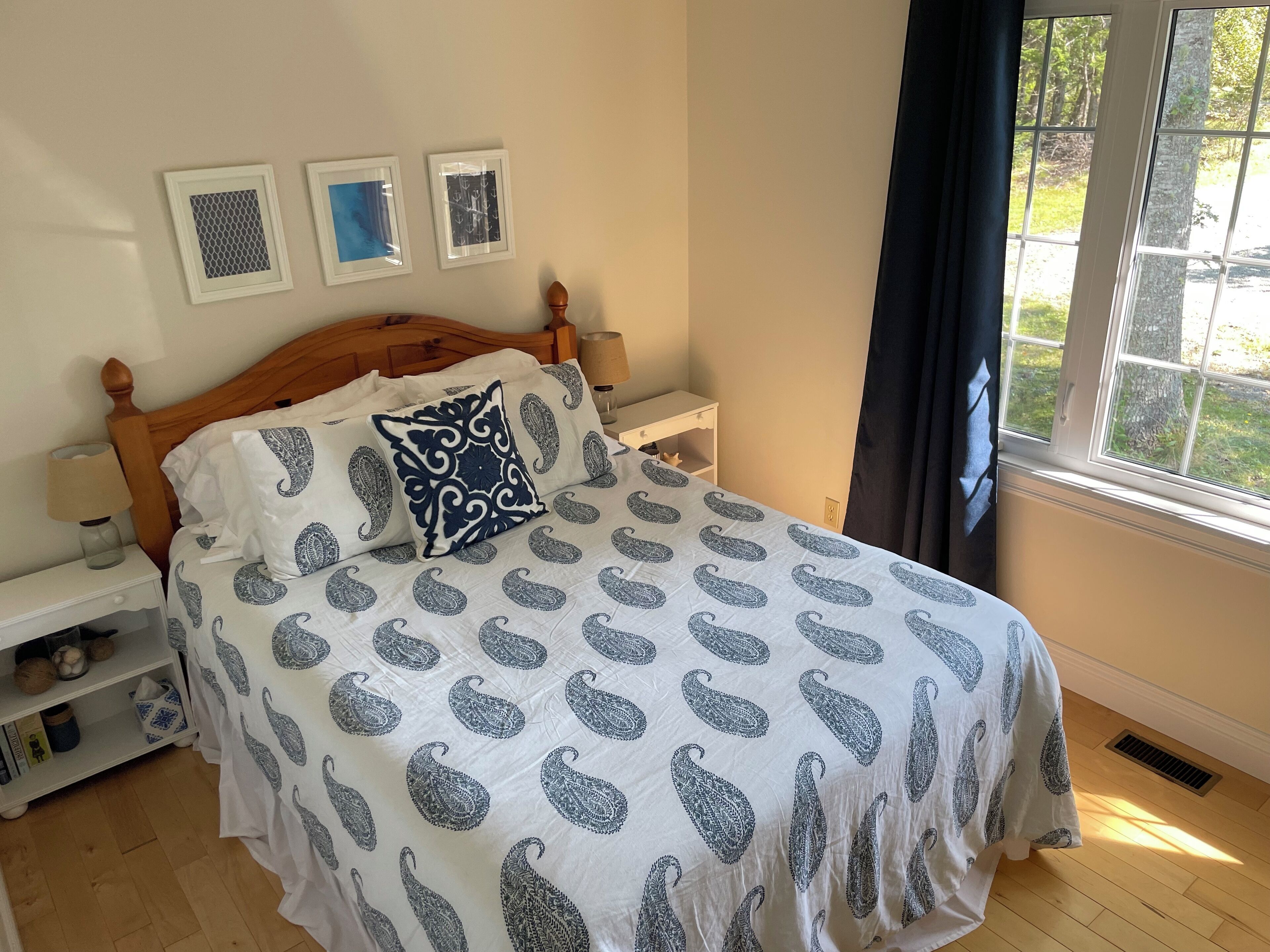 Een slaapkamer met een bed, nachtkastjes, een raam met uitzicht op groen en wanddecoratie.
