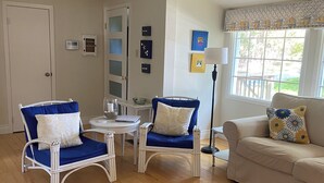 Un salon avec deux fauteuils en osier, une table basse en bois, un canapé beige et une fenêtre donnant sur l’extérieur.