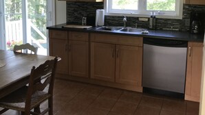 Une cuisine avec des meubles en bois, un plan de travail noir, un lave-vaisselle et une fenêtre donnant sur un espace verdoyant.