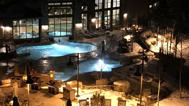 A heated outdoor pool area with stone structures and lounge chairs, surrounded by snow.
