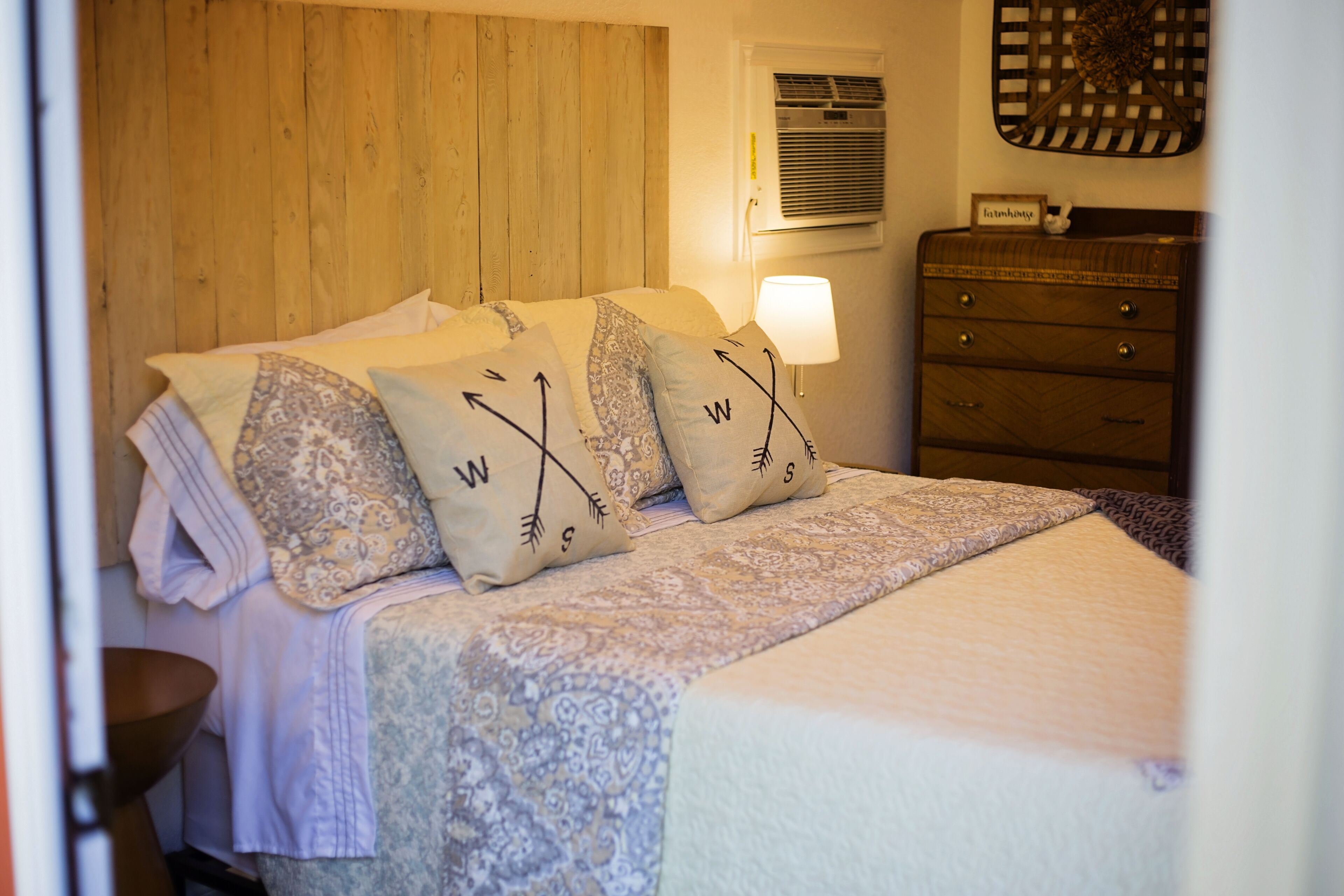 Cama bem arrumada com almofadas estampadas e abajur.