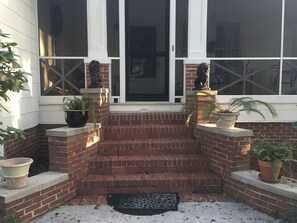 A brick staircase leading to a porch with potted plants and a black doormat.