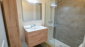 A modern bathroom with a wooden vanity, a large mirror, a glass shower enclosure, and a toilet. - Balcony View Apartment by Hello Homes Sitges (Sitges)