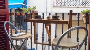 A balcony with a wooden table and two chairs, potted plants, and a blue awning in the background. - Balcony View Apartment by Hello Homes Sitges (Sitges)