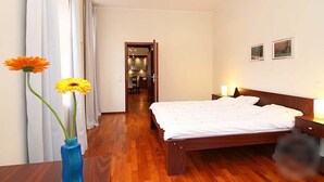 Une chambre d’hôtel avec un plancher en bois, un lit avec une literie blanche, deux lampes de chevet et un vase rempli de fleurs sur la table de chevet.