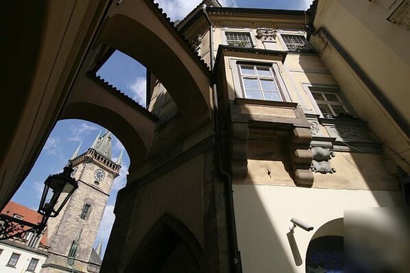 An architectural view of a building with a clock tower, arched structures, and a surveillance camera.