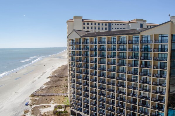 A high-rise hotel with multiple balconies overlooking a beach.