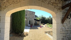 An arched stone structure leading to a stone building with a door and windows, surrounded by a gravel area and potted plants. - Gordes/Goult - Stunning Mas Provençal On A Hill In Luderon (Goult)