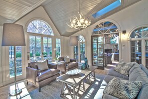 Relax in a spacious living area with a high ceiling and large windows, featuring a stone fireplace and comfortable seating.