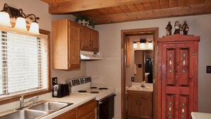 Une cuisine avec des meubles de rangement en bois, une cuisinière, un évier et une fenêtre avec des stores.