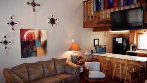 Un salon chaleureux avec un canapé marron, une table basse en bois et un téléviseur fixé à un mur en bois.